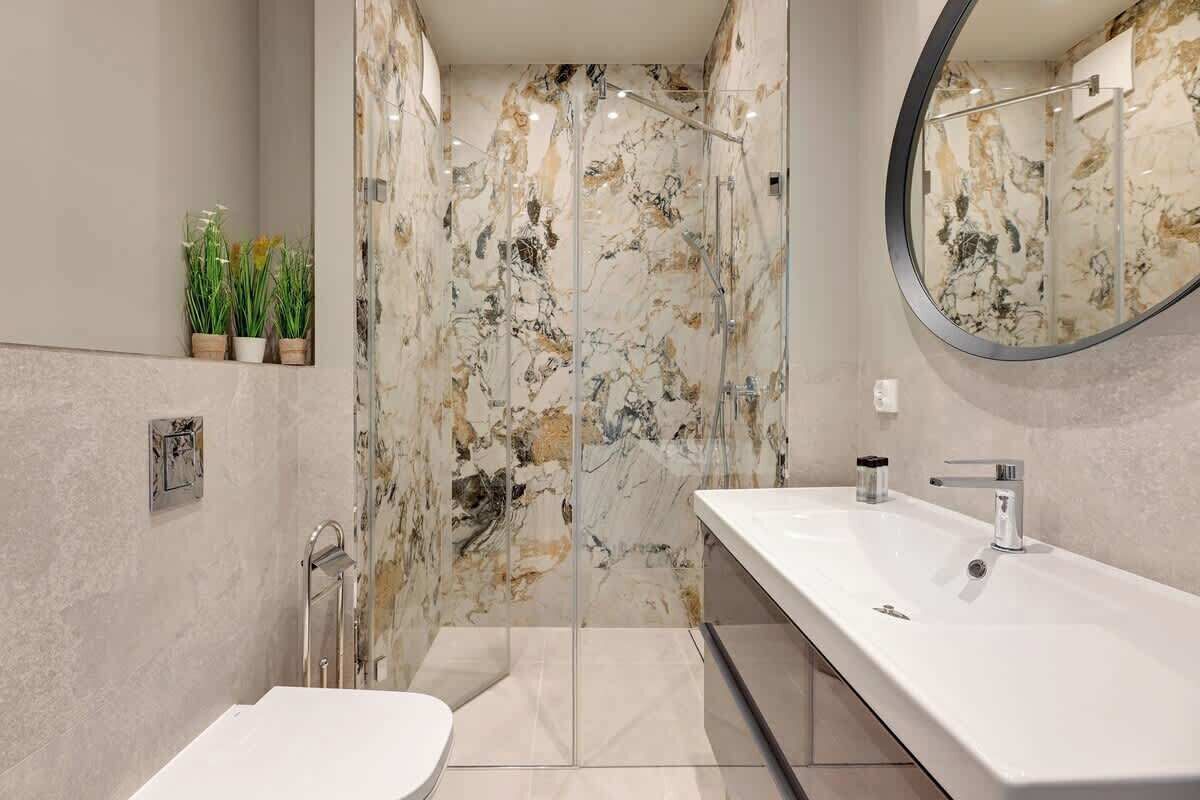 Une salle de bain moderne avec une douche en marbre, un grand miroir et un lavabo blanc.
