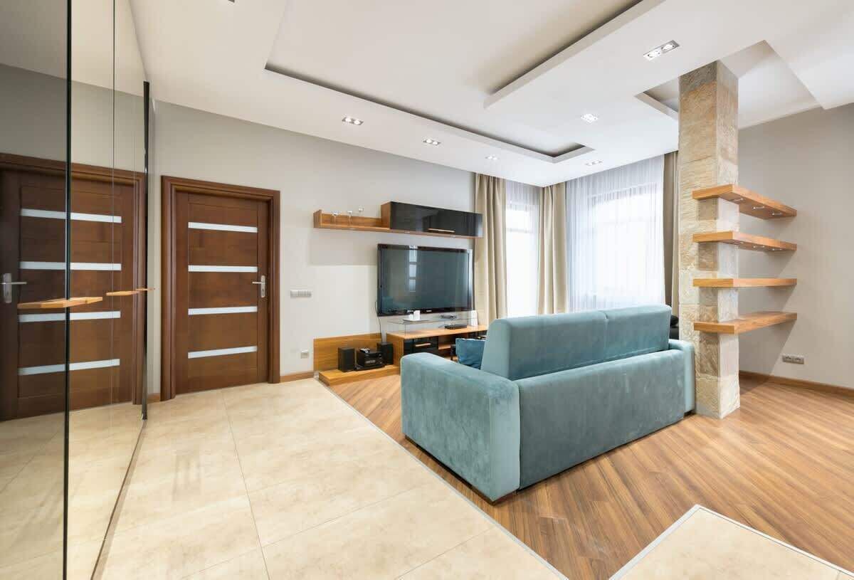 Ein modernes Wohnzimmer mit blauem Sofa, Holzboden, Flachbildfernseher und einer Glaswand.