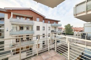 Un immeuble résidentiel à plusieurs étages, doté de balcons, d’un espace extérieur couvert et offrant une vue sur les bâtiments voisins.