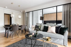 Una sala de estar moderna con un sofá gris, una mesa de comedor con sillas, una mesa de centro y un gran ventanal con cortinas.