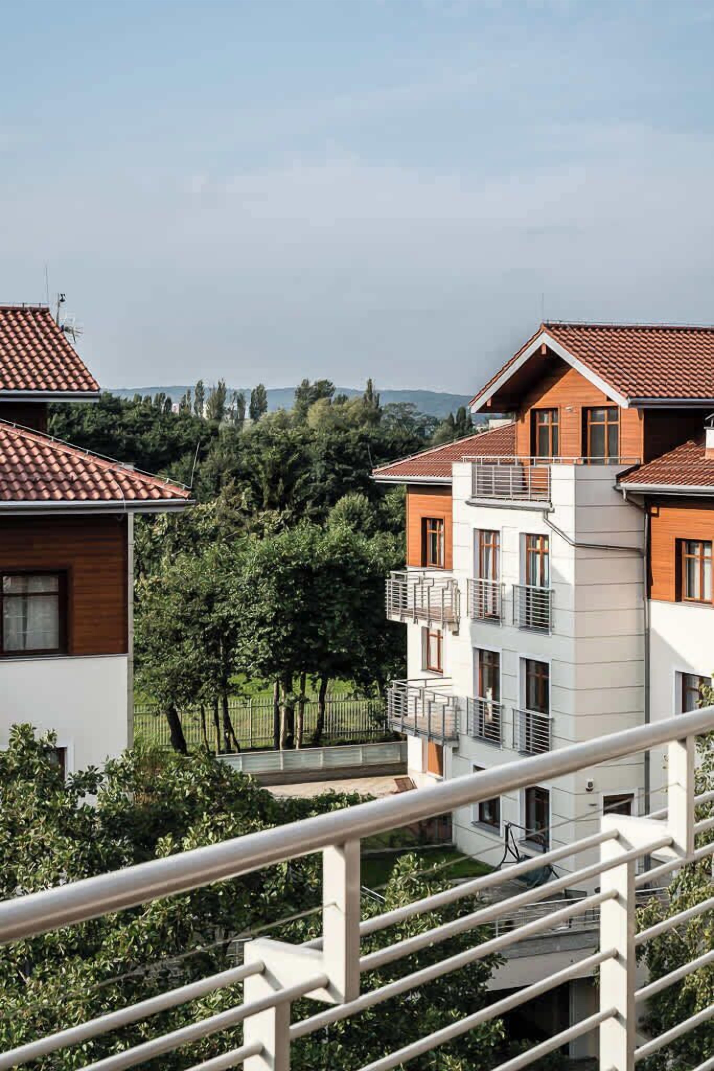 A multi-story residential building with a red-tiled roof, balconies, and a view of a lush green landscape.