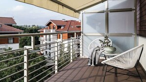 A balcony with a view of neighboring houses, a white chair, and a small table with a bowl and plant.