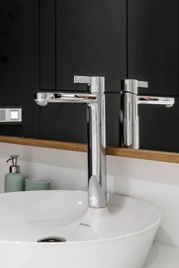 Un baño moderno con un lavamanos blanco, grifos cromados y un espejo encima.