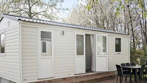 A white mobile home with a brick patio and a dining area with chairs.