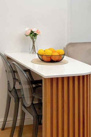 A dining table with a white surface, a wooden side panel, and a bowl of oranges. - Sunny Apartment | SPA, Balcony, 300 m to the Beach (Gdańsk)