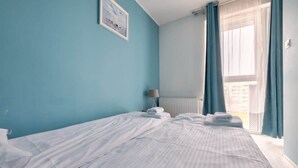 A hotel room with a large bed, a bedside table with a lamp, and a window with curtains.