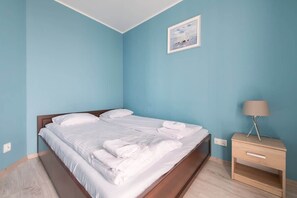 Un lit bien fait, avec du linge de lit blanc et des oreillers, une table de chevet avec une lampe, et un tableau encadré au mur.