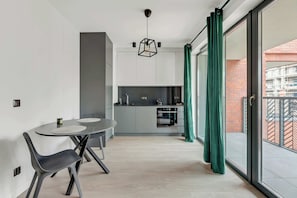 Une cuisine moderne avec des meubles gris, un four encastré et un coin repas comprenant une table ronde et des chaises.