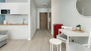 Eine moderne Küche mit weißen Schränken, einer Mikrowelle und einer Kaffeemaschine. Es gibt eine Essecke mit Tisch und Stühlen sowie einen roten Kühlschrank.