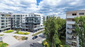 Ein moderner Wohnkomplex mit mehreren Balkonen, einem begrünten Innenhof und blauem Himmel.