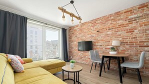 A modern living room with a yellow sofa, a small round table with a plant, and a brick wall.