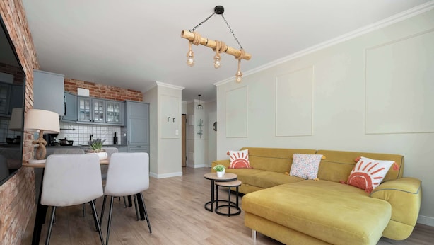 A modern living room with a sofa, chairs, a small table, and a kitchen in the background.