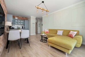 Ein modernes Wohnzimmer mit einer Couch, Sesseln, einem kleinen Tisch und einer Küche im Hintergrund.