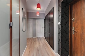 Un corridoio con pavimento in legno, una porta con carta da parati fantasia scura e una lampada a sospensione rossa.