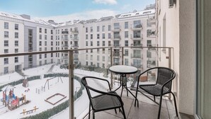 A balcony with two wicker chairs and a small table, overlooking a snow-covered playground and adjacent buildings.