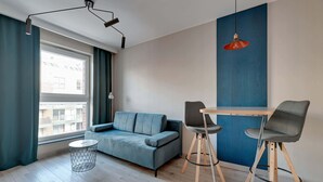 A modern living room with a sofa, two chairs, a small round table, and a hanging pendant light. - Comfortable Apartment in the Center | Remote Work (Gdańsk)