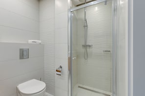 Ein modernes Badezimmer mit einer gläsernen Duschkabine, einer Toilette und einem Handtuchspender.
