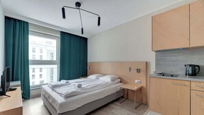Ein modernes Hotelzimmer mit Bett, Schreibtisch, Küchenzeile und einem Fenster mit Vorhängen.