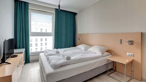 Ein modernes Hotelzimmer mit Bett, Fernseher, Schreibtisch und einem Fenster mit Vorhängen.