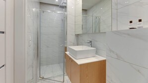 Ein modernes Badezimmer mit einer gläsernen Duschkabine, einem weißen Waschbecken und einem Holzschrank.