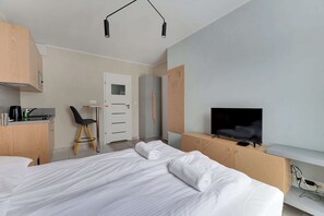 A modern hotel room with a bed, a desk with a coffee maker, a TV, and a chair.