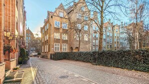 Une rue pavée bordée de bâtiments historiques, d’une haie et d’un ciel dégagé.