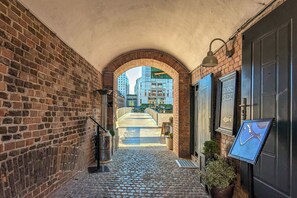 A brick corridor with a metal railing, a potted plant, and a framed sign on the wall.