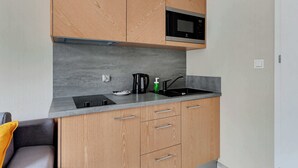 Una cocina compacta con armarios de madera, un microondas integrado, un hervidor eléctrico negro y un lavamanos moderno.