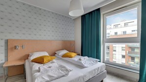 Habitación de hotel con dos camas, una ventana con cortinas, un cabecero y una lámpara colgante.