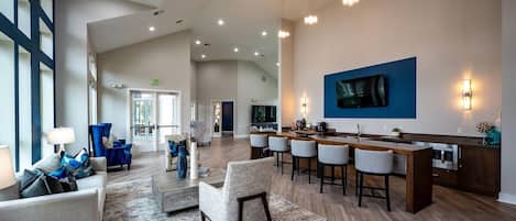 A spacious lobby with a bar area, seating, and a large TV screen.