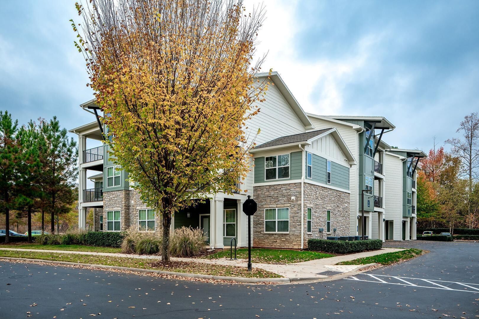 A multi-story apartment building with a stone facade, balconies, and a parking lot.