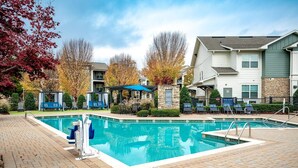 Ein rechteckiger Pool mit Backstein-Terrasse, umgeben von Liegestühlen und einem Gazebo.