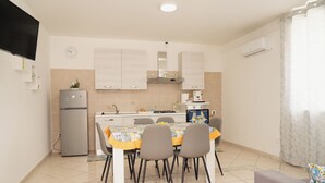 A compact kitchen with a dining table, chairs, a refrigerator, and a flat-screen TV mounted on the wall. - Cannavacciuolo house (Gragnano)