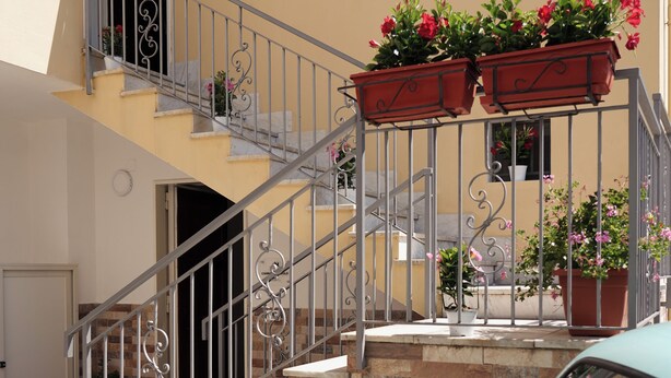 A turquoise car parked in front of a building with a staircase leading to a balcony with potted plants. - Cannavacciuolo house (Gragnano)