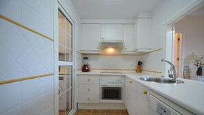 A compact kitchen with white cabinets, a built-in oven, a sink, and a window with blinds. - La Marina 1 5 - Two Bedroom Apartment, Sleeps 5 (Punta del moral)