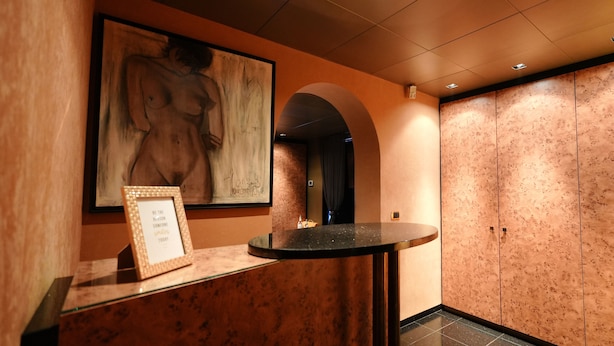A reception area with a framed artwork, a reception desk, and a large arched doorway leading to a room with a patterned wall. - Relax Gent Wellness (Lievegem)
