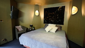 A hotel room with a bed, a chair, a nightstand, a lamp, and a wall-mounted TV. - Relax Gent Wellness (Lievegem)