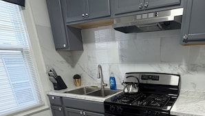 Une cuisine avec des armoires grises, une hotte de cuisinière en acier inoxydable, une cuisinière à gaz, un four encastré et un évier à deux bacs.