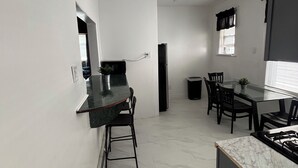 Une cuisine moderne avec un plan de travail en marbre, un coin repas doté d’une table en verre et un réfrigérateur noir.