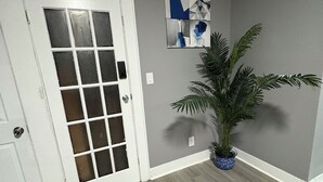 Un couloir avec une porte blanche, une plante en pot et une œuvre d’art abstraite accrochée au mur.