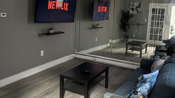Un salon moderne avec un grand téléviseur à écran plat fixé au mur, une table basse en bois foncé et un canapé bleu à motifs.