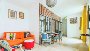 Un salon moderne avec un mur d’accent en briques, un coin repas avec des chaises bleues et un canapé orange vif.