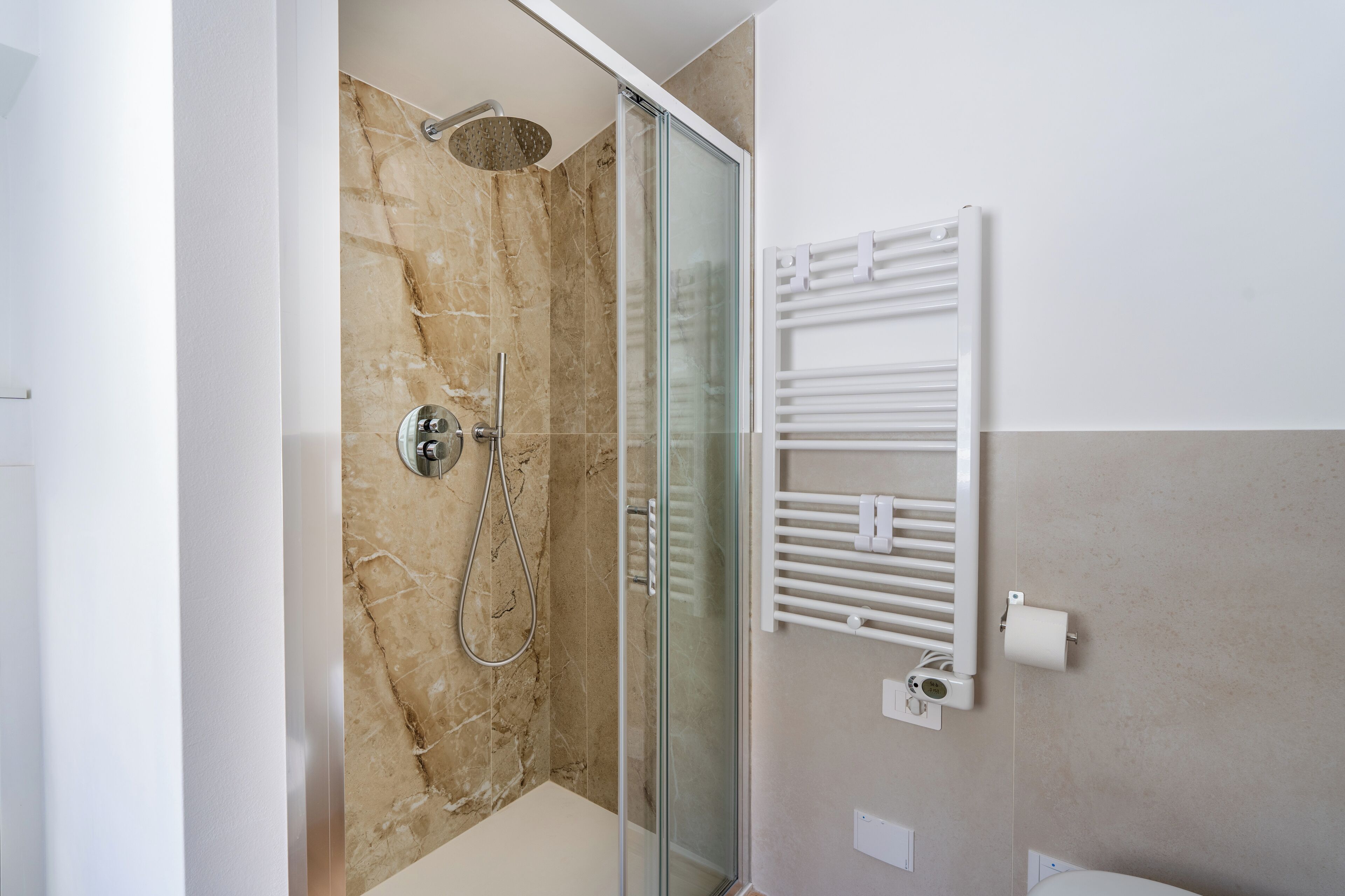 Une salle de bain moderne avec une douche à parois de verre, un porte-serviettes blanc et un mur en marbre.