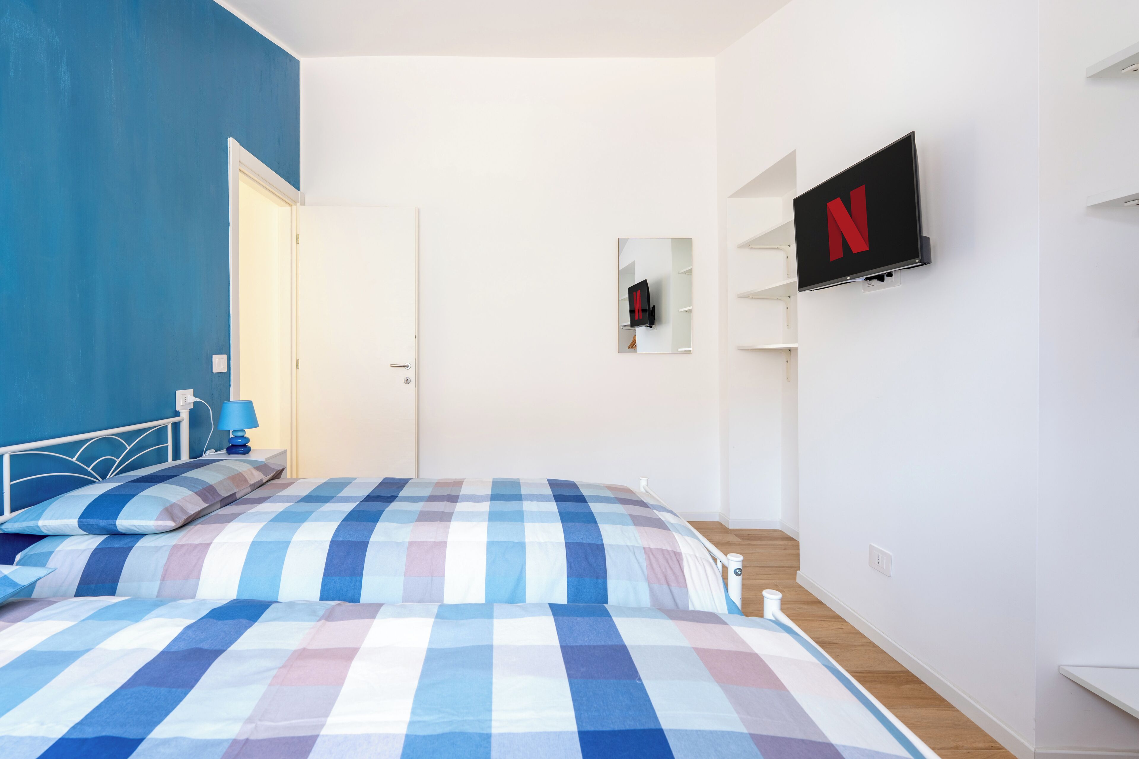 A bedroom with a checkered bedspread, a TV mounted on the wall, and a door leading to another room.