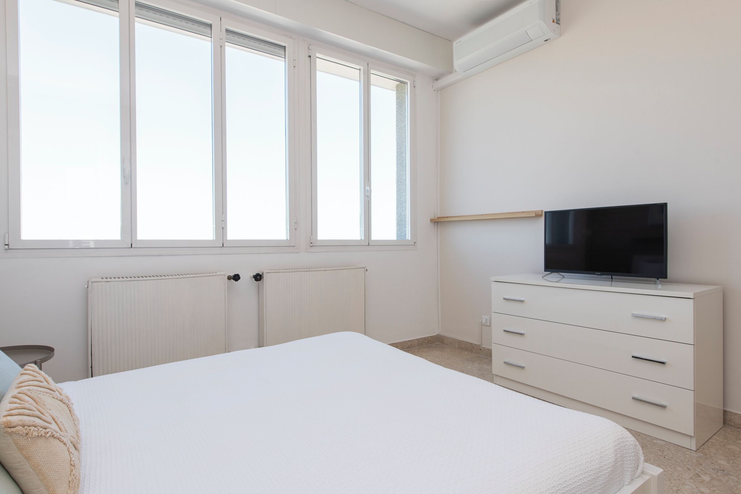 A bedroom with a bed, a TV on a dresser, and a window with blinds.