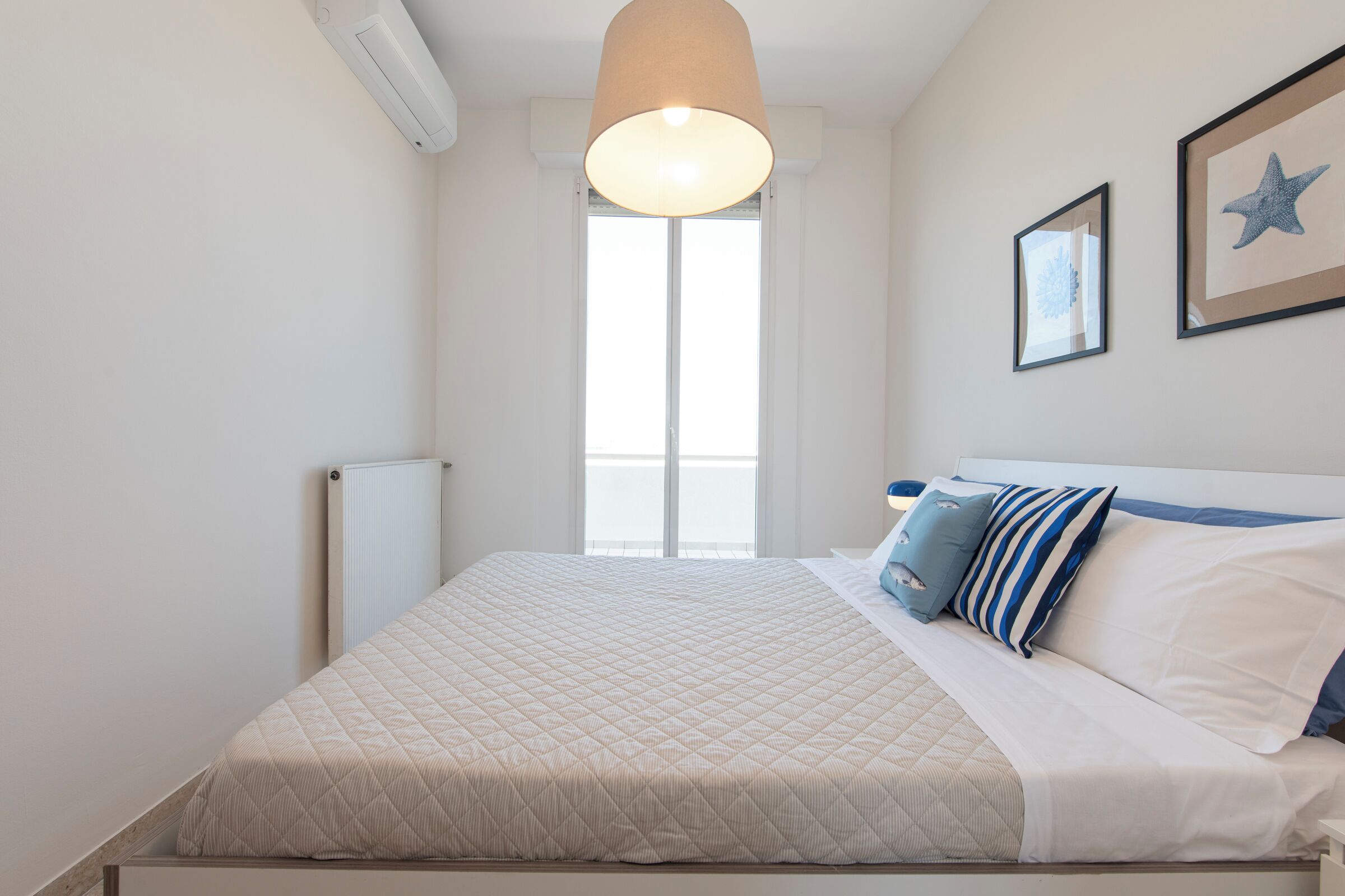A neatly made bed with a quilted cover, a hanging light fixture, and a framed star decoration on the wall.