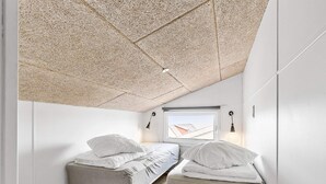Une petite chambre moderne avec deux lits simples, une fenêtre donnant sur un beau paysage et un plafond en pente.