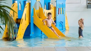 Un espace de jeux aquatiques avec un toboggan et des structures d’escalade sur le thème d’un château, le tout situé dans une piscine intérieure.