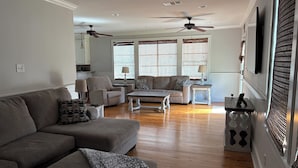 A living room with a sofa, armchair, and coffee table, a dining area with a table and chairs, and a kitchen in the background. - Spacious 5-bedroom house in charming Bay St. Louis with WiFi, AC (Bay St. Louis)