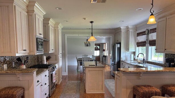 A spacious kitchen with white cabinetry, a central island, and a dining area in the background. - Spacious 5-bedroom house in charming Bay St. Louis with WiFi, AC (Bay St. Louis)